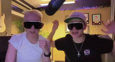 two people wearing sunglasses and hats are standing next to each other in a room .