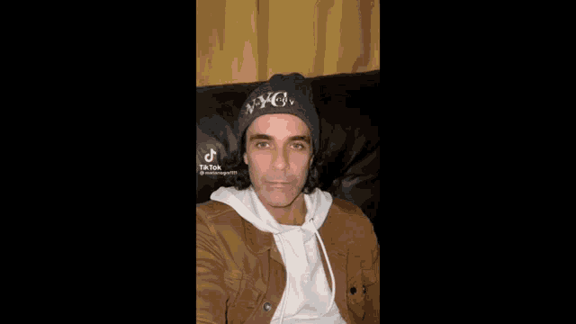 a man wearing a beanie is sitting on a couch and making a funny face .