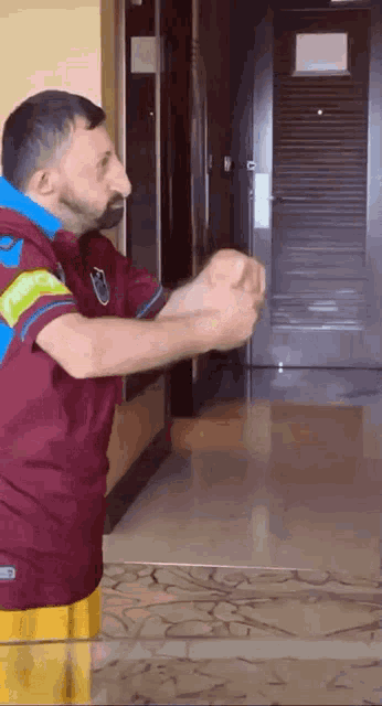 a man in a maroon shirt is standing in front of a door with his arms outstretched