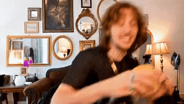 a man is sitting on a couch holding a candle in a living room with mirrors on the wall .