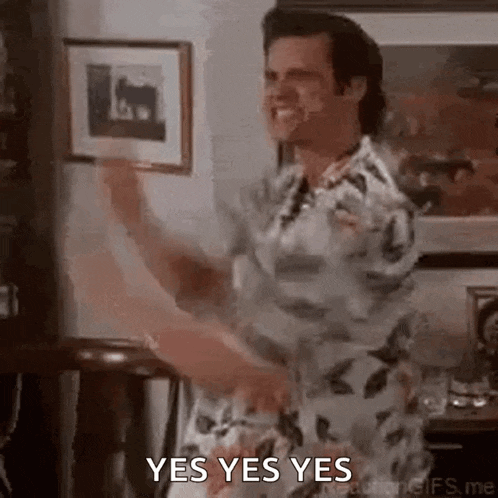 a man is dancing in a living room while holding a framed picture and saying yes yes yes .