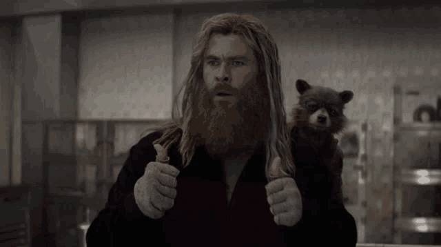 a man with a beard is giving a thumbs up next to a raccoon