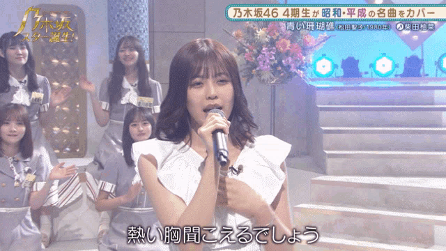a woman singing into a microphone with chinese writing on the bottom right
