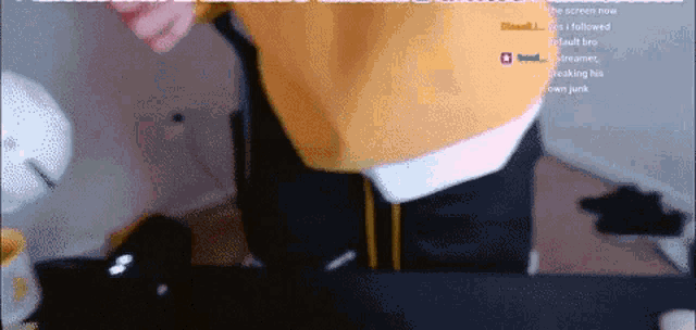 a man in a yellow sweater is standing in front of a computer screen with a streamer 's name in the corner