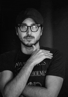 a man wearing glasses and a hat is wearing a holmes shirt