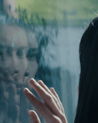 a woman 's face is reflected in a window and her hand is touching it