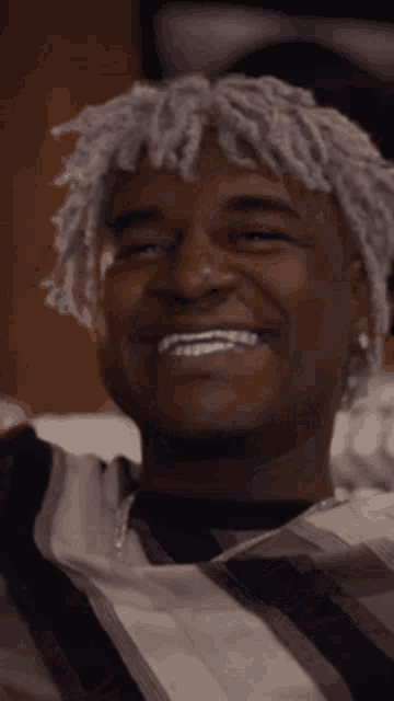 a man with purple hair is smiling and wearing a striped shirt