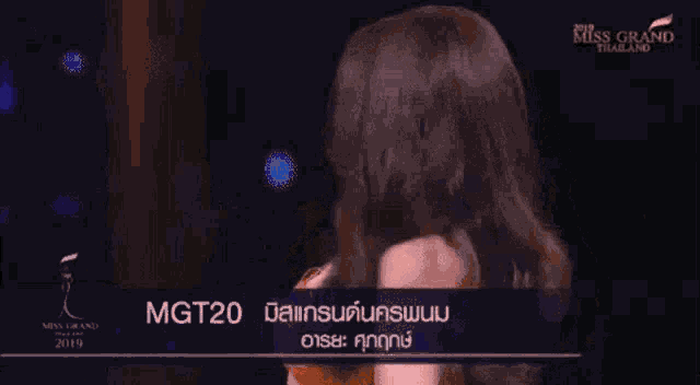 a miss grand thailand contestant smiles while wearing an orange dress