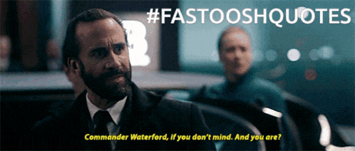 a man in a suit and tie talks to commander waterford