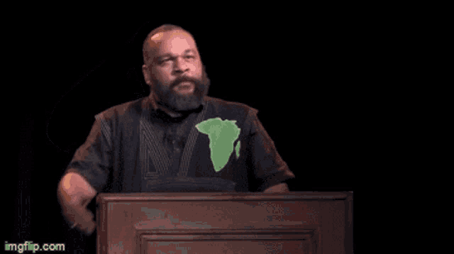 a man wearing a black shirt with a green map of africa salutes while standing at a podium
