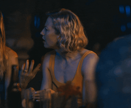 a woman in a yellow tank top sits at a table with other people