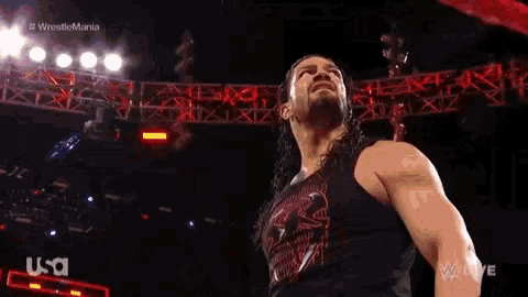 roman reigns is holding a wrestling championship belt in front of a crowd of people .