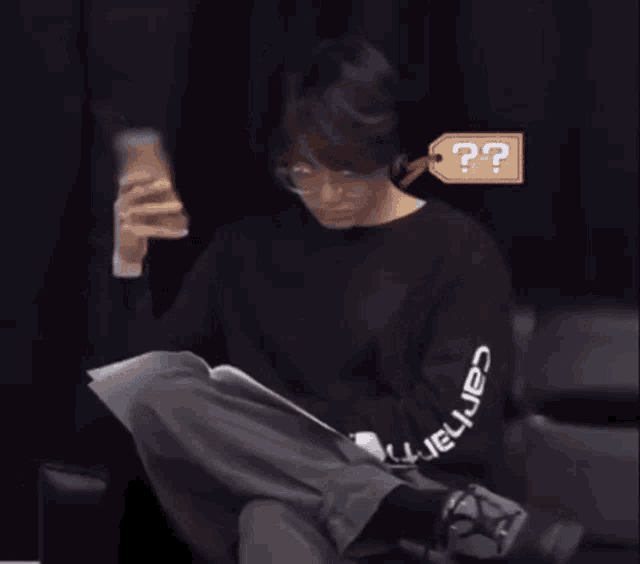 a man wearing a black carhartt sweatshirt sits on a chair reading a book