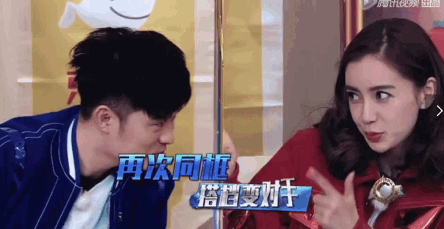 a man and a woman are standing next to each other and the woman is pointing at the man 's face .