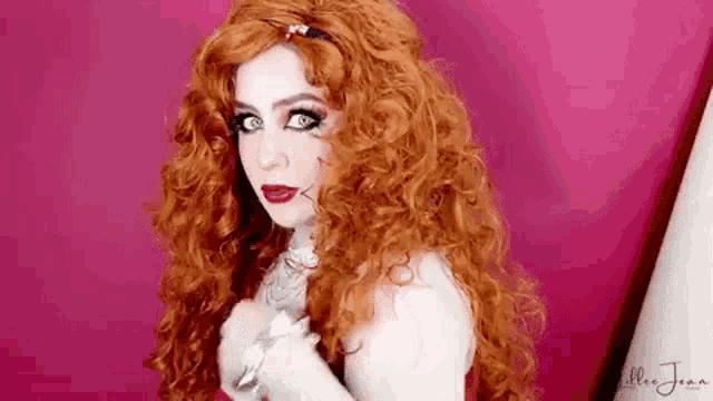 a woman with red hair and green eyes is wearing a red dress and a wig .