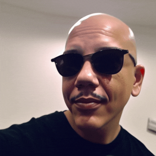 a bald man wearing sunglasses and a black shirt smiles for the camera