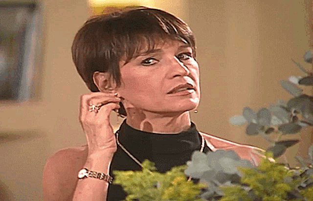a woman wearing earrings and a watch is standing in front of a bouquet of flowers