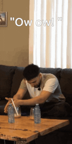 a man is sitting on a couch holding a straw in front of a table with bottles of water on it ..