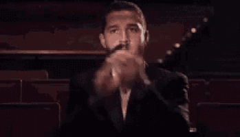 a man in a tuxedo and bow tie is clapping his hands in an auditorium .