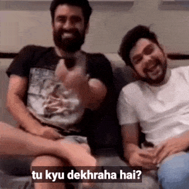 two men are sitting on a couch with a caption that says tu kyu dekharha hai ?