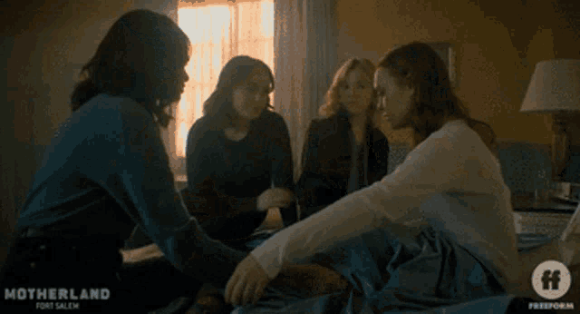 a group of women sitting on a bed with motherland fort salith on the bottom