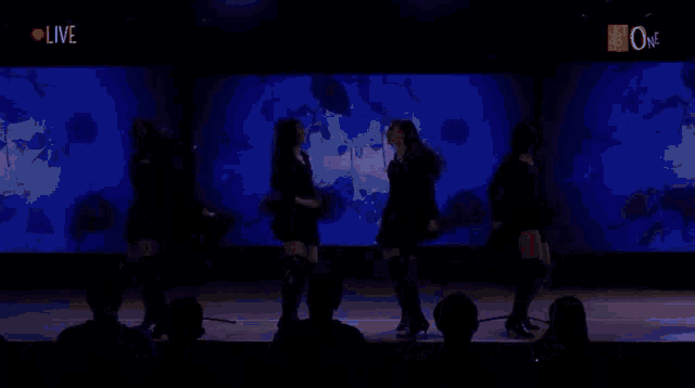 a group of women are dancing on a stage in front of a blue background that says live