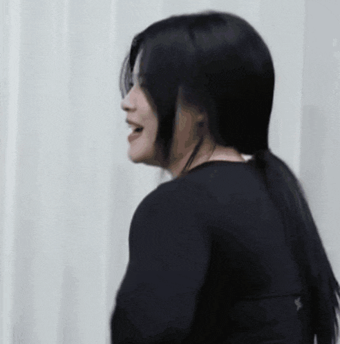 a woman with long black hair is wearing a black shirt and smiling .