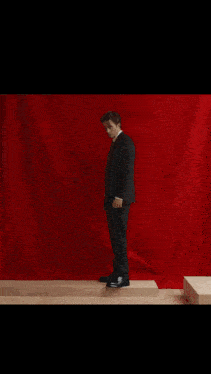 a man in a suit and tie is dancing in a room with a red curtain behind him .