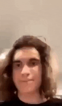 a young man with long hair is looking at the camera .