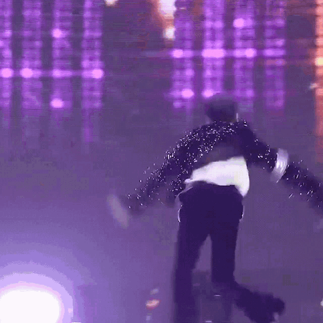 a man in a black and white sequined jacket is dancing on a stage with purple lights behind him