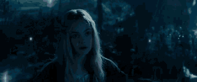a woman with long blonde hair is standing in a dark forest surrounded by purple lights .