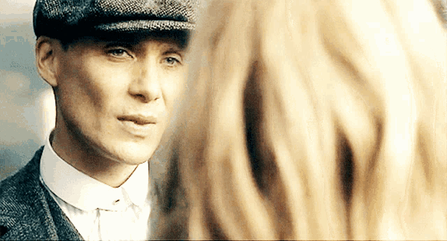 a man wearing a hat and a suit looks at a woman