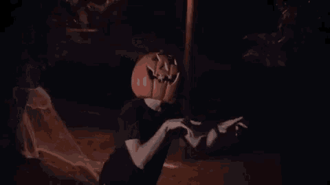 a man wearing a pumpkin on his head is standing in the dark .