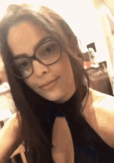 a woman wearing glasses and a black top is taking a selfie