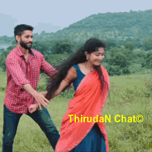 a man in a plaid shirt is holding a woman in a red saree in a field .