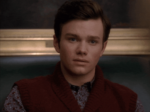 a young man wearing a red sweater vest and a floral shirt