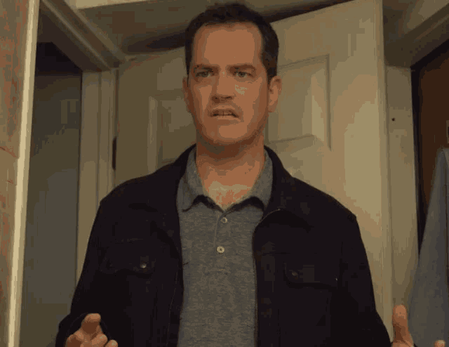 a man wearing a black jacket and a grey shirt stands in front of a door