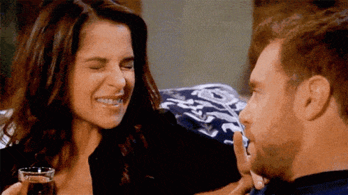 a man and a woman are sitting next to each other and the woman is laughing while the man is touching her face .