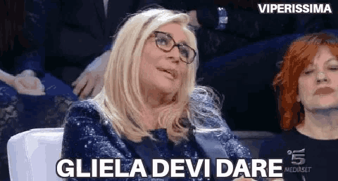 a woman wearing glasses is sitting in a chair in front of a microphone and saying gliela devi dare .