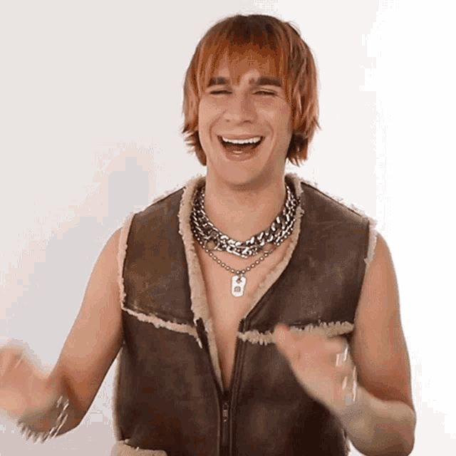 a man wearing a brown vest and a necklace with the letter b