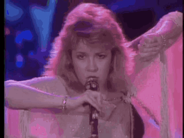 a woman is singing into a microphone in a pink dress .