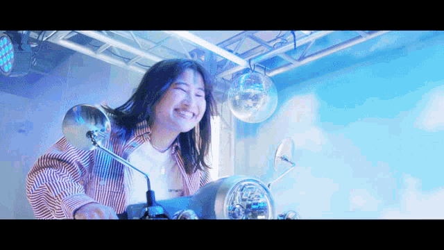 a woman is smiling while riding a motorcycle with a disco ball behind her
