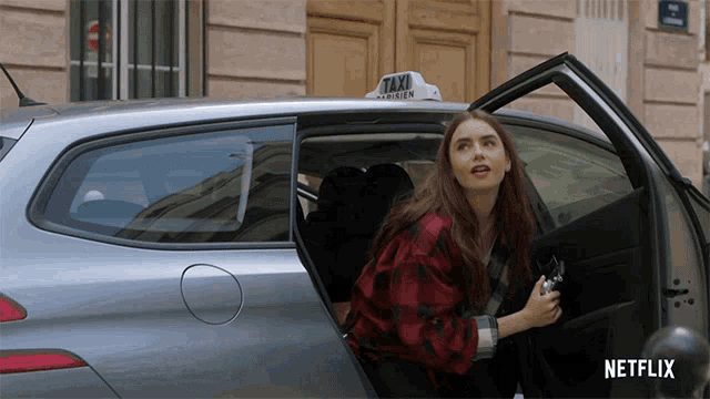 a woman in a red plaid shirt is getting out of a silver taxi