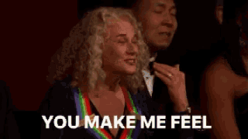 a woman in a rainbow necklace is sitting next to a man in a tuxedo and says `` you make me feel ''