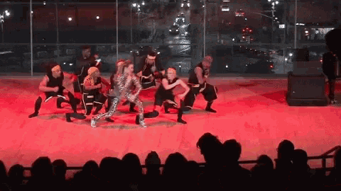 a group of people are dancing on a stage in front of a large crowd
