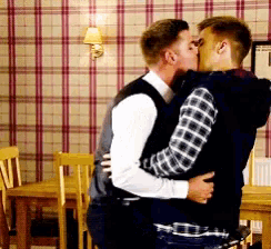 two men are kissing in a room with plaid wallpaper