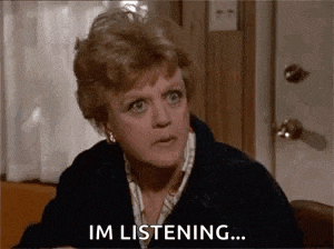 a woman is sitting at a table talking to someone and saying `` i 'm listening '' .