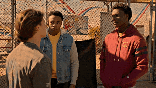 a man wearing a red hoodie with the word champion on it talks to two other men