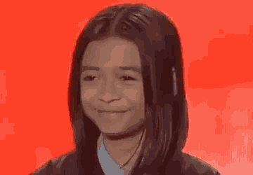 a little girl is smiling in front of a red background .