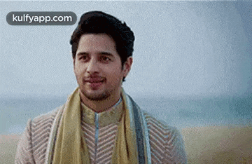 a man wearing a scarf around his neck is standing on a beach and smiling .